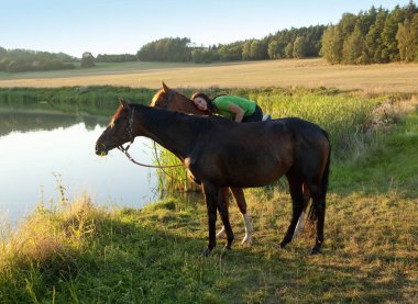 Bir gölün yanında iki at ile kadın kucaklamaları