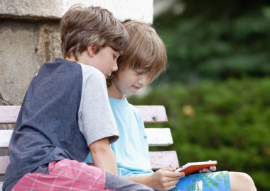 Tablet ile oynarken bankta oturan iki çocuk