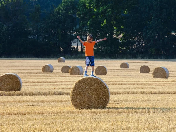 Menino escalando um fardo de feno em um campo — Fotografia de Stock