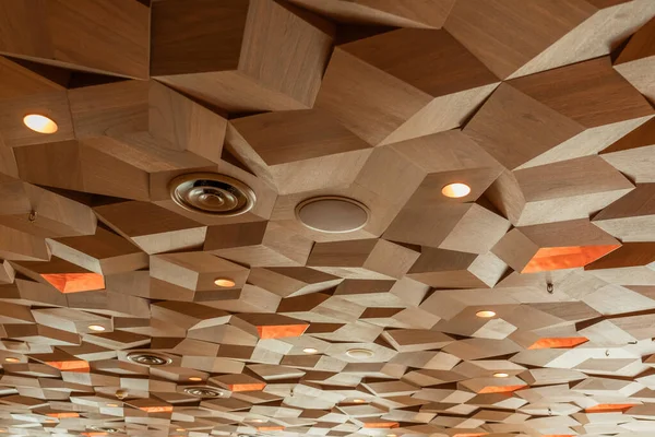 Lights Speakers Ventilation and Fire Sprinklers on Drop Ceiling Wooden Texture Tiles. Hexagon Metal Timber Panels. Three Dimensional Cube Shape Decoration.