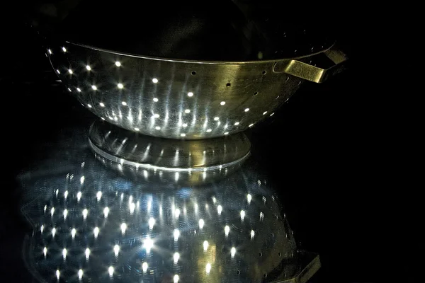 Colander de prata com reflexão de luzes na bancada no escuro — Fotografia de Stock