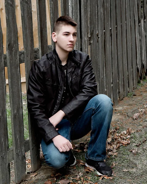 High School male Sitting by Wooden Fence in Black Leather Jacke — Stock Photo, Image