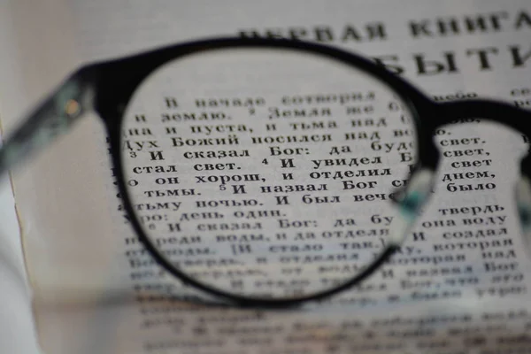 First verses of Genesis in the Orthodox Bible seen through glasses, close-up.