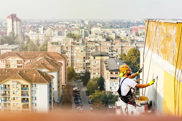 Ouvrier d'accès à la corde industrielle accroché au bâtiment tout en peignant le mur extérieur de la façade. Image concept d'alpinisme industriel. Vue du dessus — Photo