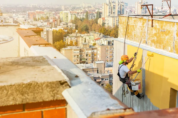 Ouvrier d'accès à la corde industrielle accroché au bâtiment tout en peignant le mur extérieur de la façade. Image concept d'alpinisme industriel. Vue du dessus — Photo