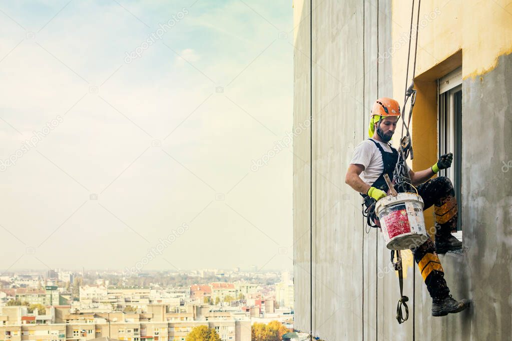 Industrial rope access worker hanging from the building while painting the exterior facade wall. Industrial alpinism concept image. Top view