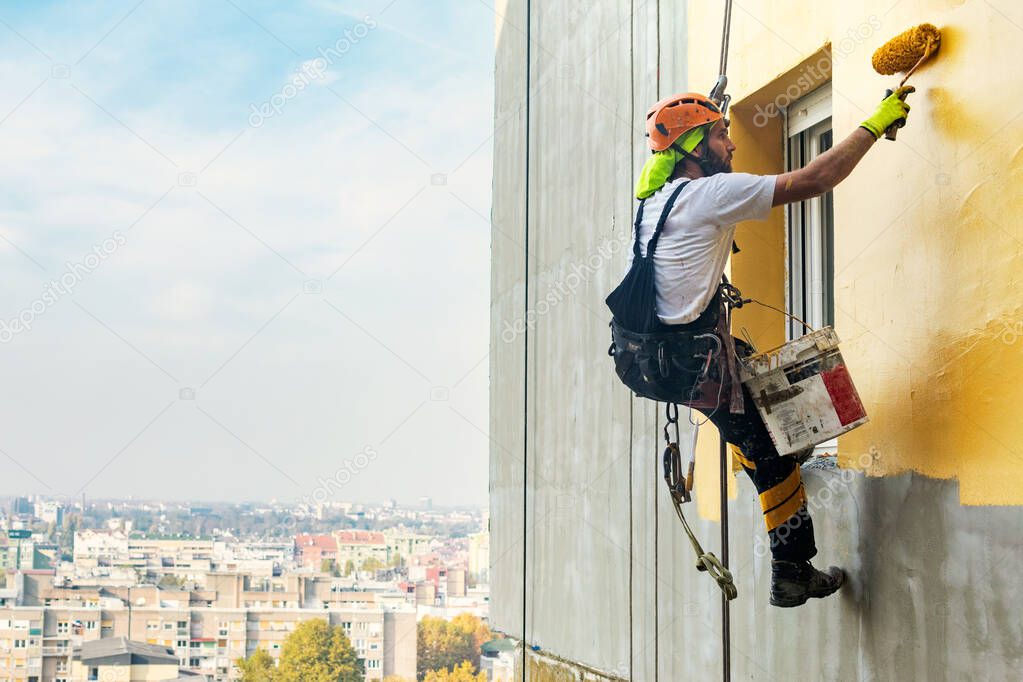 Industrial rope access worker hanging from the building while painting the exterior facade wall. Industrial alpinism concept image. Top view