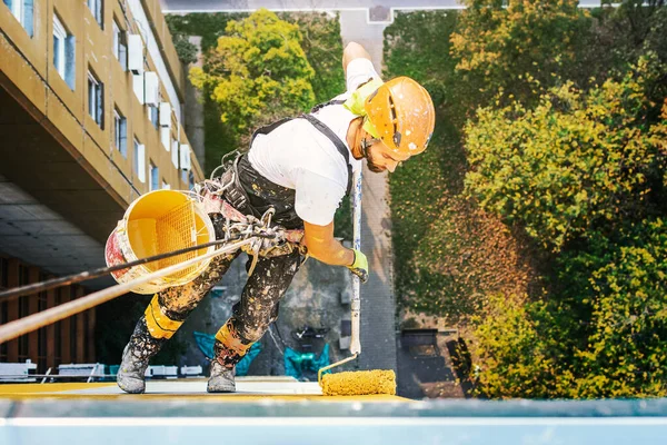 Ouvrier d'accès à la corde industrielle accroché au bâtiment tout en peignant le mur extérieur de la façade. Image concept d'alpinisme industriel. Vue du dessus — Photo