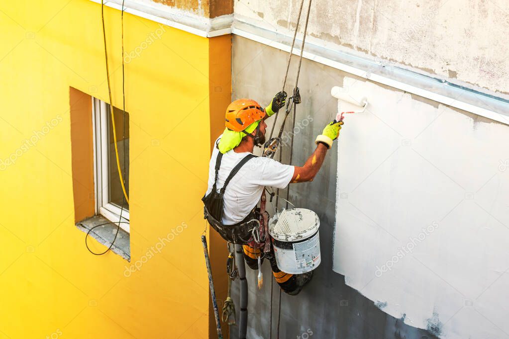 Industrial rope access worker hanging from the building while painting the exterior facade wall. Industrial alpinism concept image. Top view