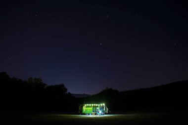 Gece vakti sahilde klasik bir karavan. Parlayan yıldızlı karanlık yıldızlı gökyüzü. Kampçı yaşam tarzı