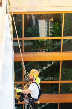 Endüstriyel dağcı uzun apartmanın dış cephesini boyarken ipte asılı duruyor. Endüstriyel yükseklik ve yüksek riskli iş yeri konsept görüntüsü