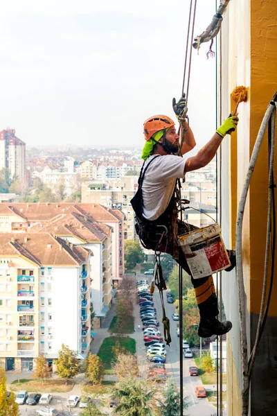 Endüstriyel dağcı uzun apartmanın dış cephesini boyarken ipte asılı duruyor. Endüstriyel yükseklik ve yüksek riskli iş yeri konsept görüntüsü