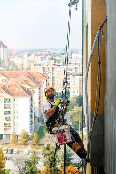 Endüstriyel dağcı uzun apartmanın dış cephesini boyarken ipte asılı duruyor. Endüstriyel yükseklik ve yüksek riskli iş yeri konsept görüntüsü