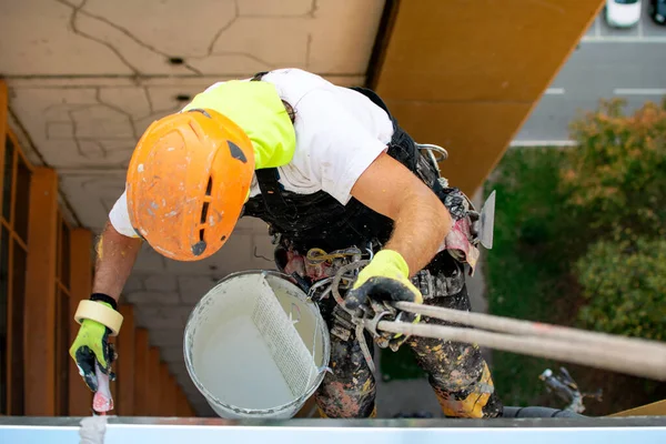 Industrial climber hanging on the rope while painting the exterior facade wall of the tall apartment building. Industrial alpinism and high risk work scene concept image. Top view