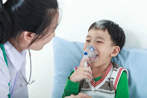 Asian boy having respiratory illness helped by health professional with inhaler.