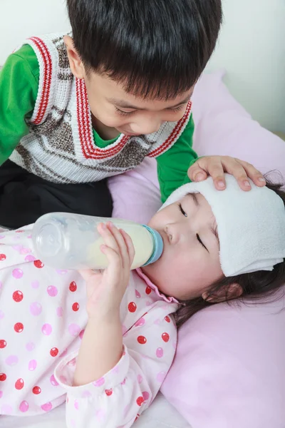 Sorella malata sdraiata e succhiare il latte sul letto, gentilmente fratello tenere la veglia su un malato di strettamente . — Foto Stock
