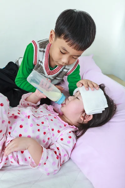 Kranke Schwester liegt und saugt Milch auf dem Bett, gütiger Bruder wacht über einen Kranken von nah. — Stockfoto