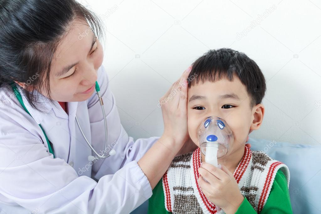 Asian boy having respiratory illness helped by health professional with inhaler.