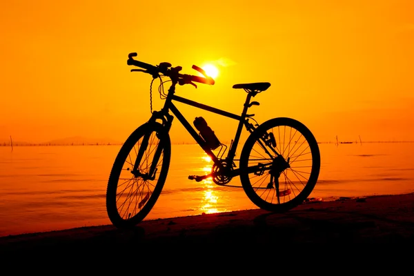 目に色鮮やかな夕焼けをビーチで自転車のシルエット — ストック写真