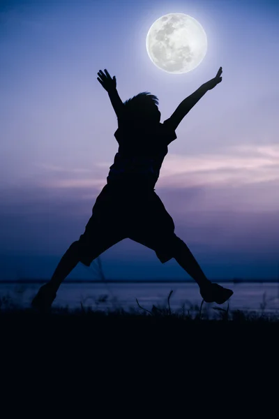 Silhouette back view of child enjoying and jumping at riverside. — Stock Photo, Image