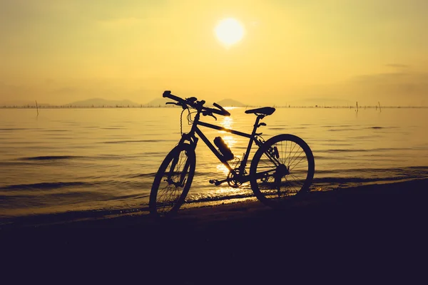 Silhueta de bicicleta na praia contra o pôr do sol colorido em th — Fotografia de Stock