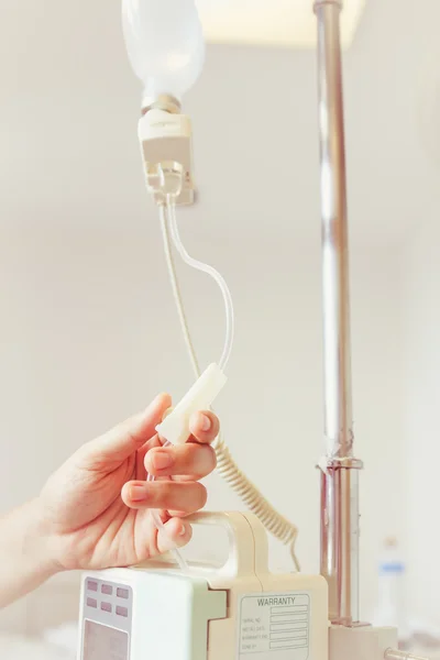 Nurse's hands regulation an intravenous (IV) drip in hospital room
