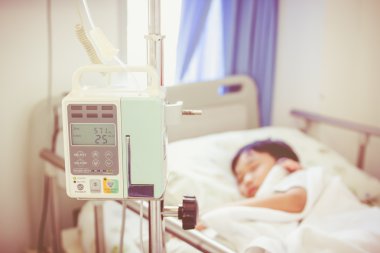Asyalı çocuk hasta yatağının üzerinde infüzyon pompa intravenöz IV damlalıkla yalan.