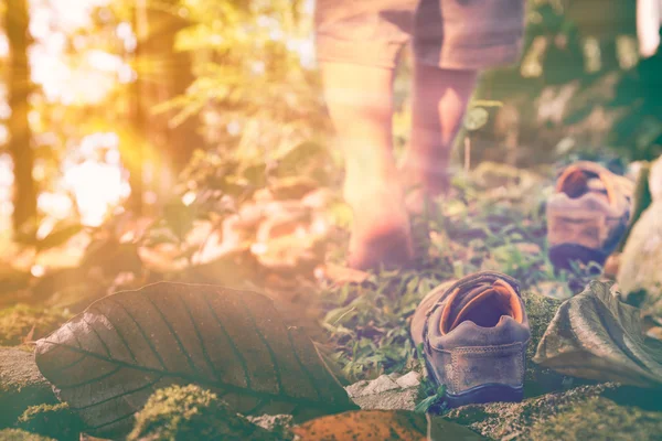 Child take off leather shoes, child's foot learns to walk on grass with bright sunlight, reflexology massage.