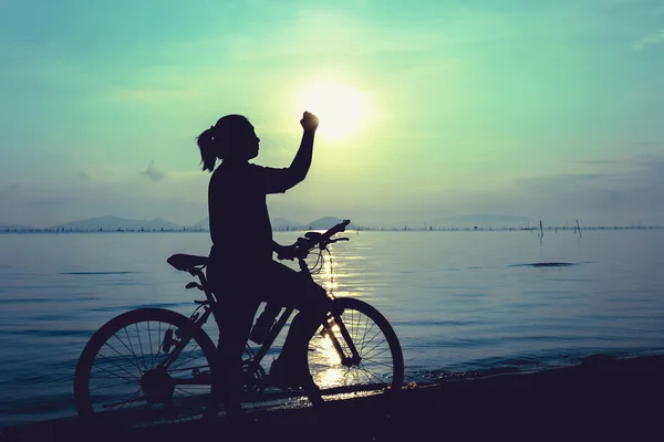 快乐女声与山地自行车在色彩斑斓的蓝色天空背景下的剪影. — 图库照片