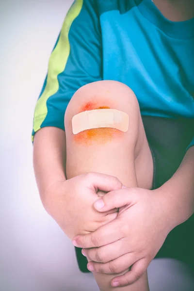 Niño atleta herido. Rodilla infantil con yeso y moretones. Tono vintage . — Foto de Stock