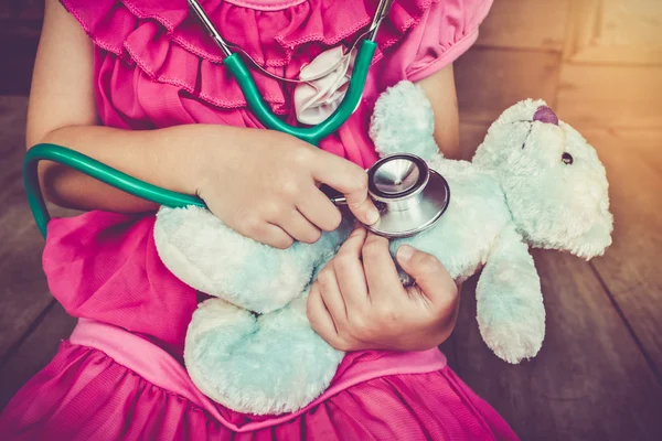 Child playing doctor or nurse with plush toy bear at home. Vintage tone.