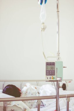 Asyalı çocuk hasta yatağının üzerinde infüzyon pompa intravenöz IV damlalıkla yalan