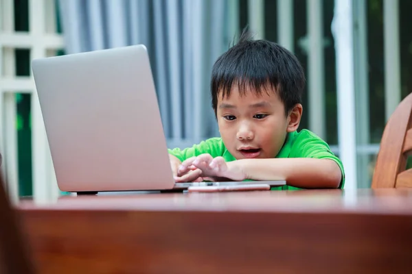 Menino asiático desfrutando de tecnologias de geração moderna jogando dentro de casa usando computador portátil e telefone celular . — Fotografia de Stock
