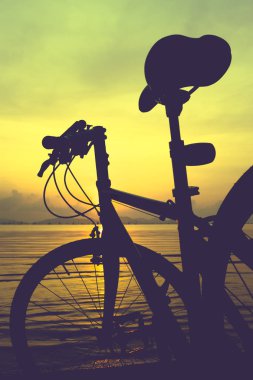 Denizin içinde renkli günbatımı karşı sahilde Bisiklet silüeti.