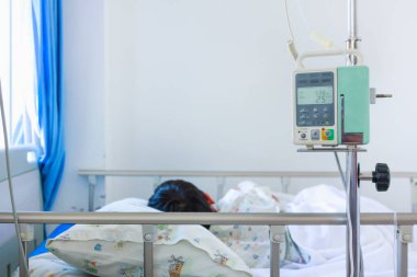 Asyalı çocuk hasta yatağının üzerinde infüzyon pompa intravenöz IV damla ile uyku