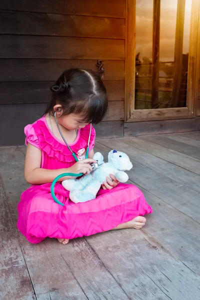 Чарівна азіатська дівчина грає у лікаря або медсестру з плюшевим іграшковим ведмедем — стокове фото