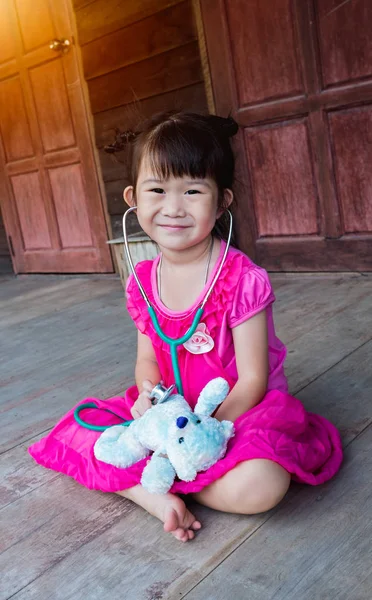 Child playing doctor or nurse with plush toy bear at home.