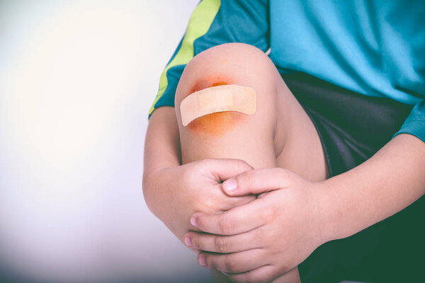 Athlete child injured. Child knee with a plaster and bruise.