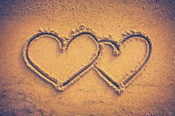 Two hearts handwritten on seashore sand. Vignette and vintage tone
