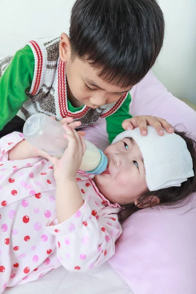 Zieke zus liggen en zuigen up melk op het bed, vriendelijk broer nachtwake houden over een ziek van nauw. — Stockfoto