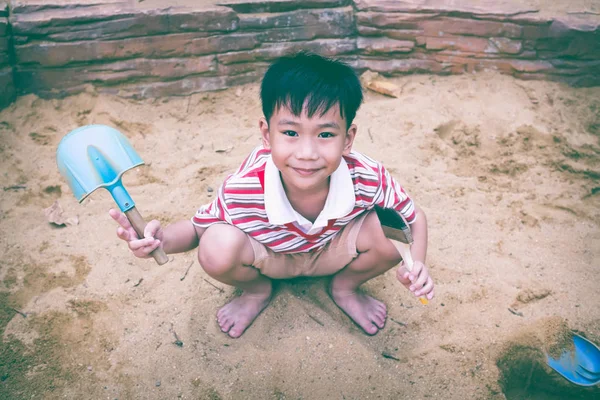 Очаровательный азиатский мальчик веселится, копаясь в песке в летний день . — стоковое фото