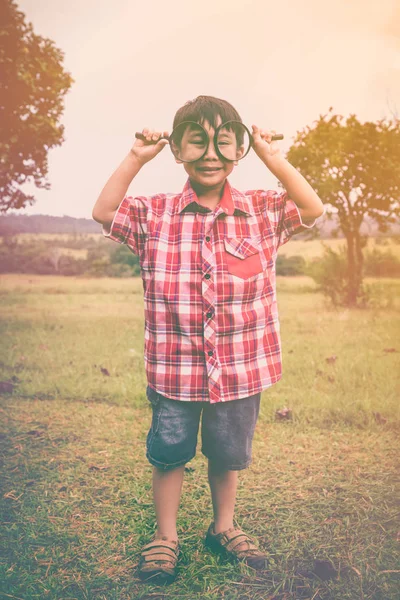 Asian child with magnifying glass at park on vacation. Education concept. — Stock Photo, Image