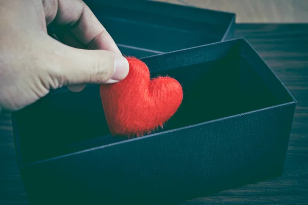 Рука людини тримає або кладе червону форму серця в чорну подарункову коробку . — стокове фото