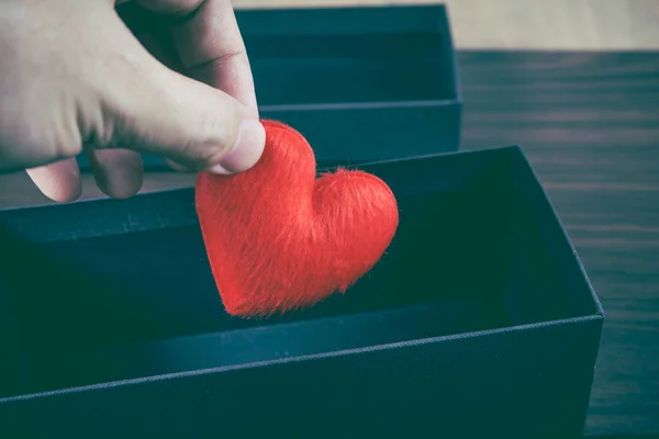 Human hand holding or putting a red heart-shaped in a black gift box. — Stock Photo, Image