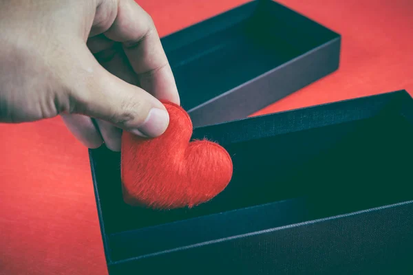 Human hand holding or putting a red heart-shaped in a black gift box — Stock Photo, Image