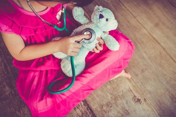 Criança brincando de médico ou enfermeira com urso de pelúcia em casa. Efeito de tom vintage . — Fotografia de Stock