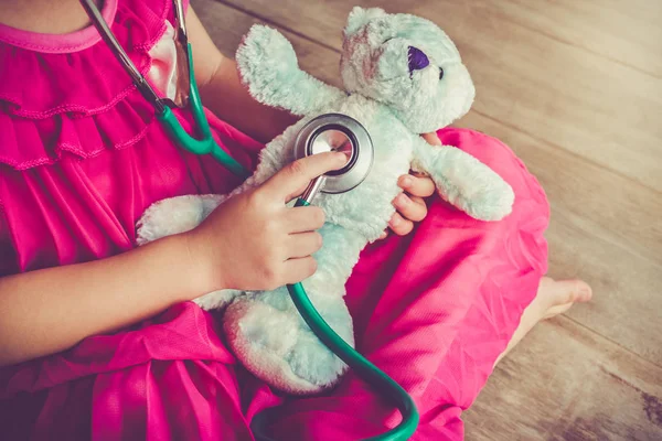 Barn leker läkare eller sjuksköterska med plysch leksak Björn hemma. Vintage tonen effekt. — Stockfoto