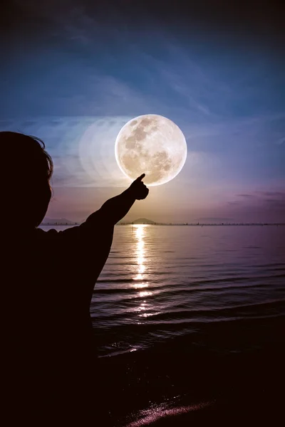 Achteraanzicht van het silhouet van de vrouw ontspannen aan de kust en wordt gewezen op de maan — Stockfoto