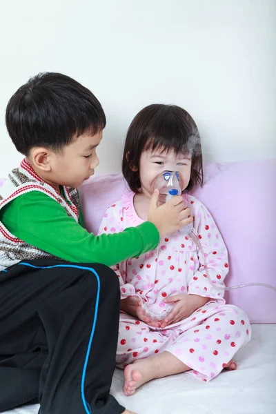 Asian girl having respiratory illness helped by brother with inhalation by mask at hospital. — Stock Photo, Image