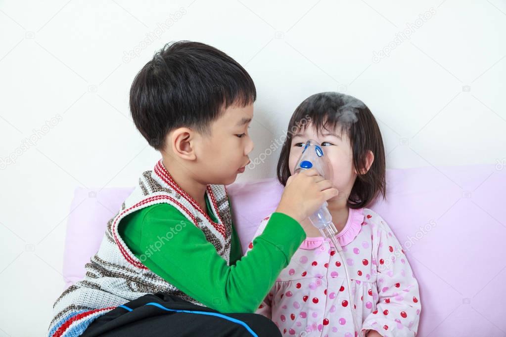 Asian girl having respiratory illness helped by brother with inhalation by mask at hospital.